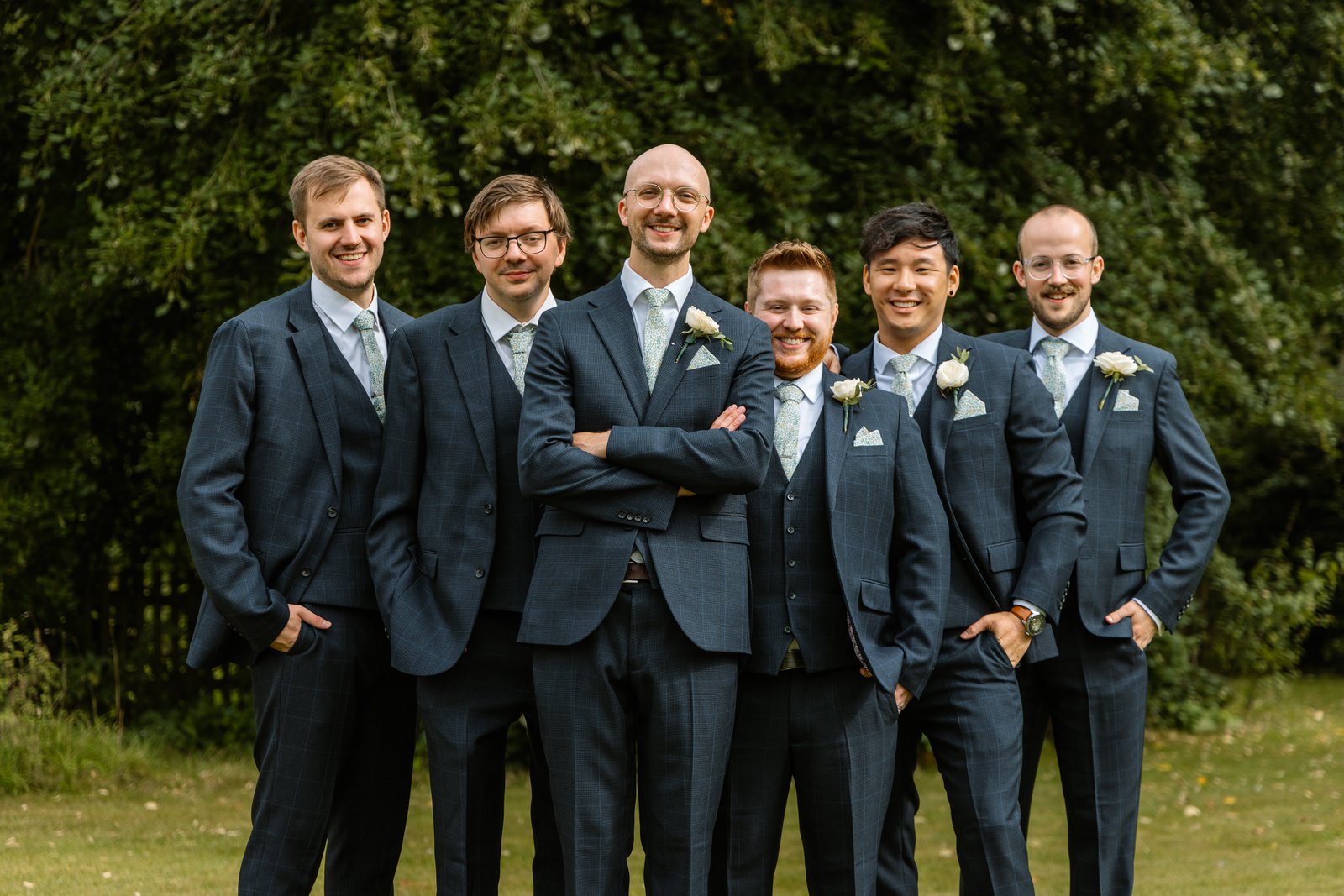 Groom standing with his groomsmen in navy three-piece suits and sage ties.