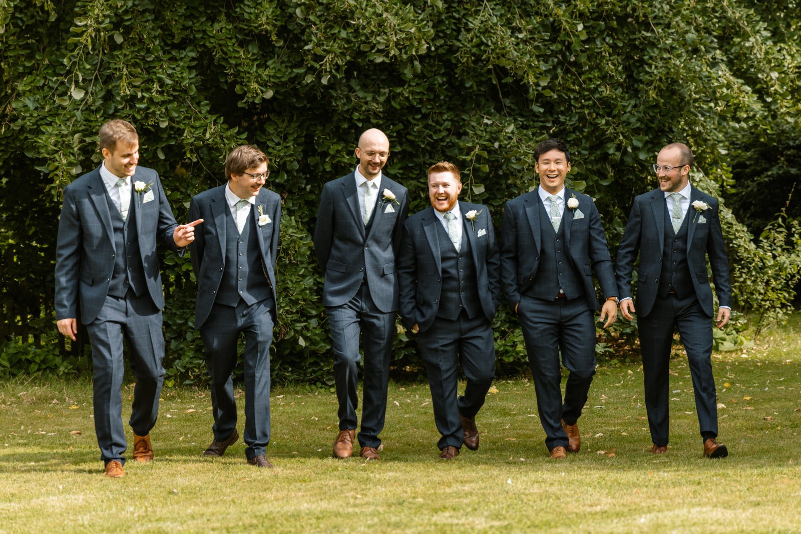 Groomsmen walking across the lawn together at Worton Hall.