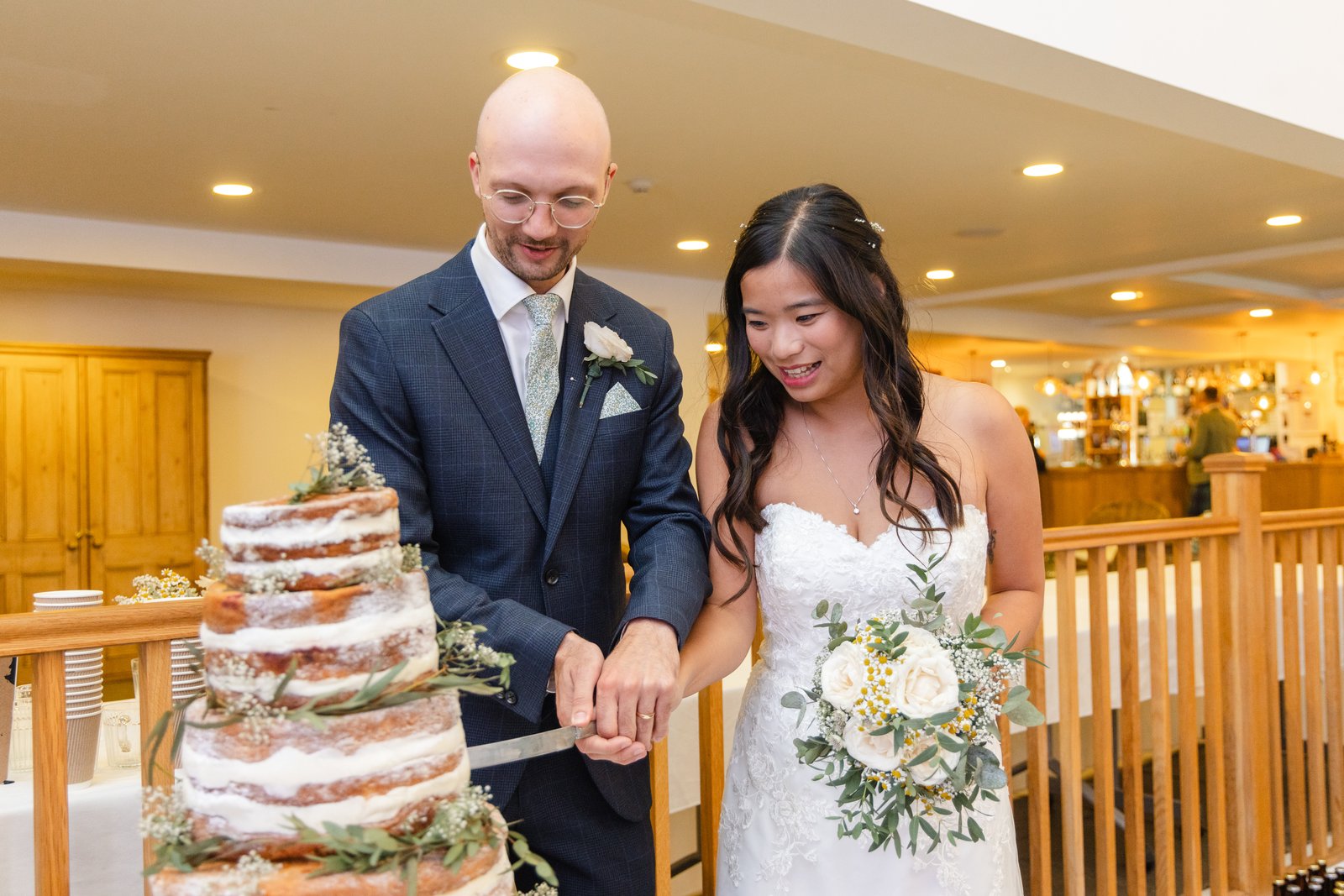 Bride and groom cutting a naked wedding cake beside the bar in the main hall.