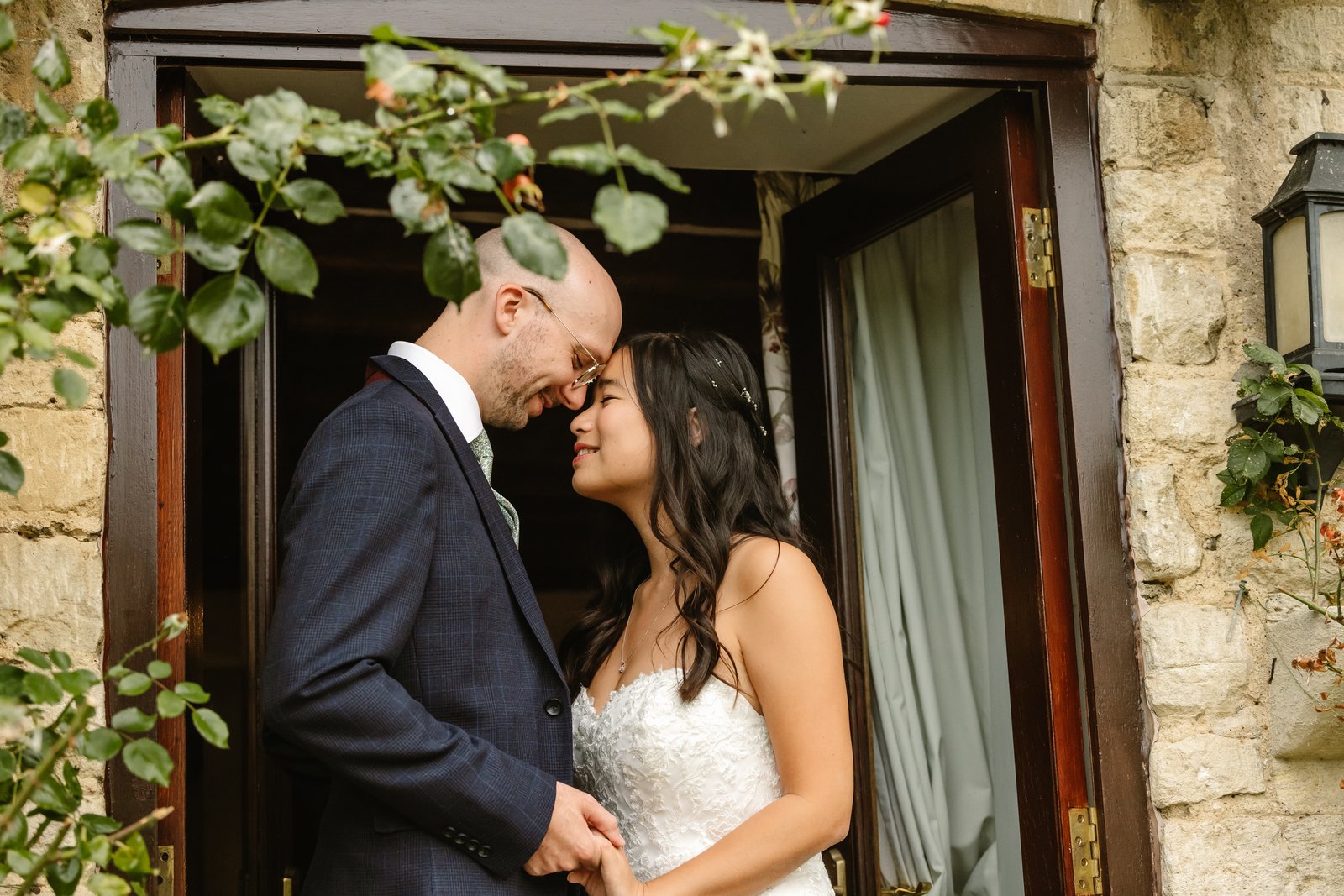 Bride and groom forehead to forehead in a stone doorway framed by climbing greenery at Worton Hall.