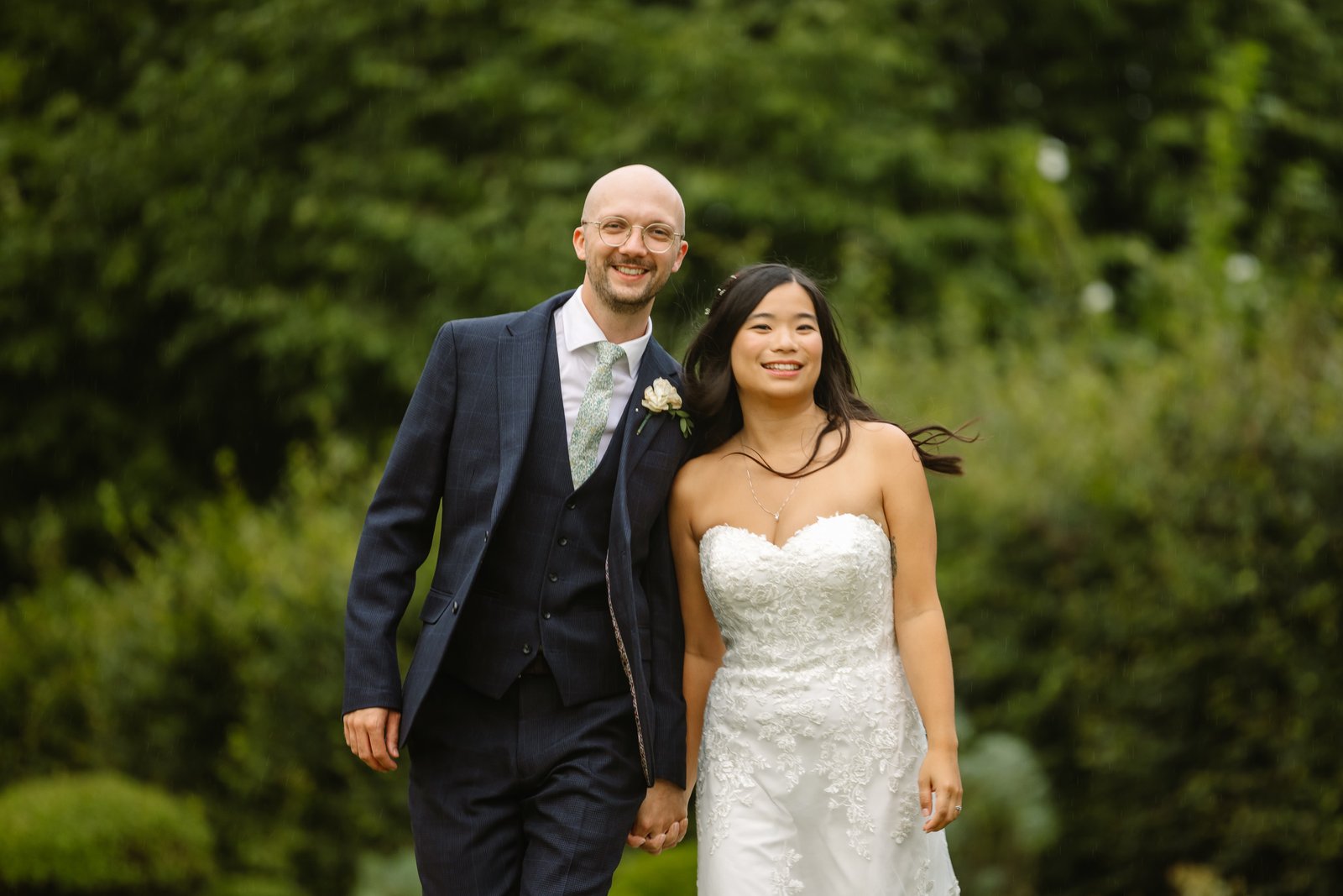 Bride and groom walking hand in hand through the gardens at Worton Hall.