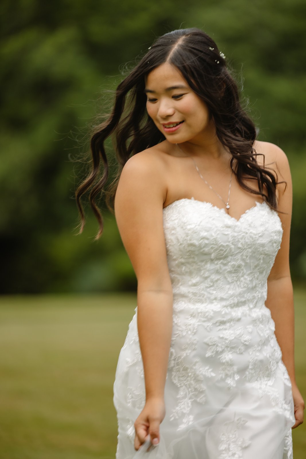 Bride smiling on the lawn at Worton Hall in a strapless lace gown.