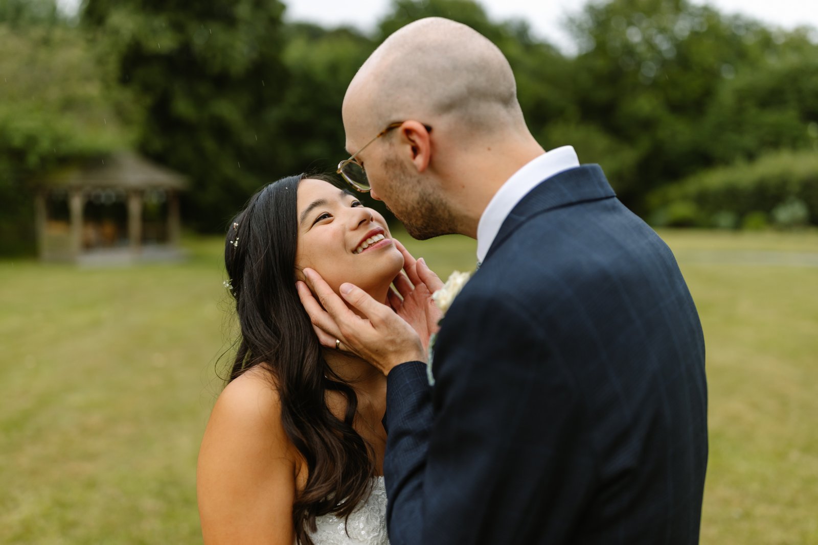 Groom cupping the bride's face on the lawn, the wooden garden gazebo visible behind them.