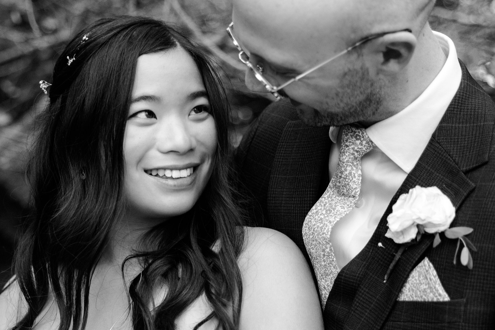 Black and white close portrait of the bride smiling as the groom leans his head towards her.