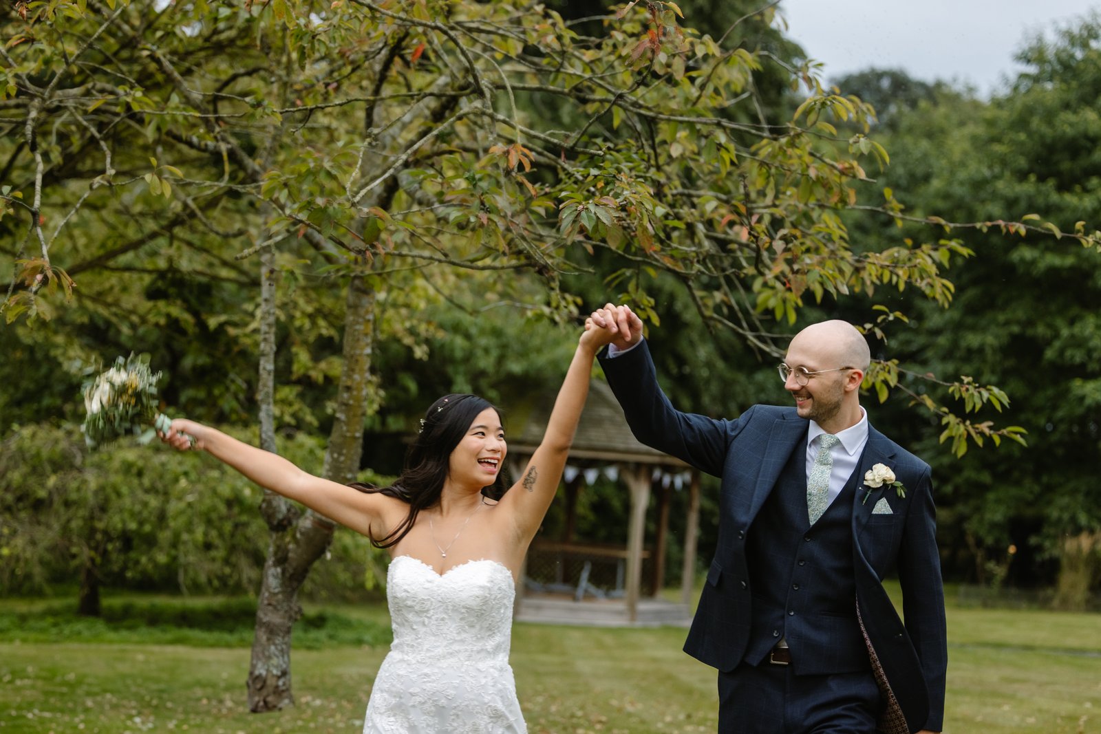 Bride and groom dancing together on the grass beneath a spreading tree.