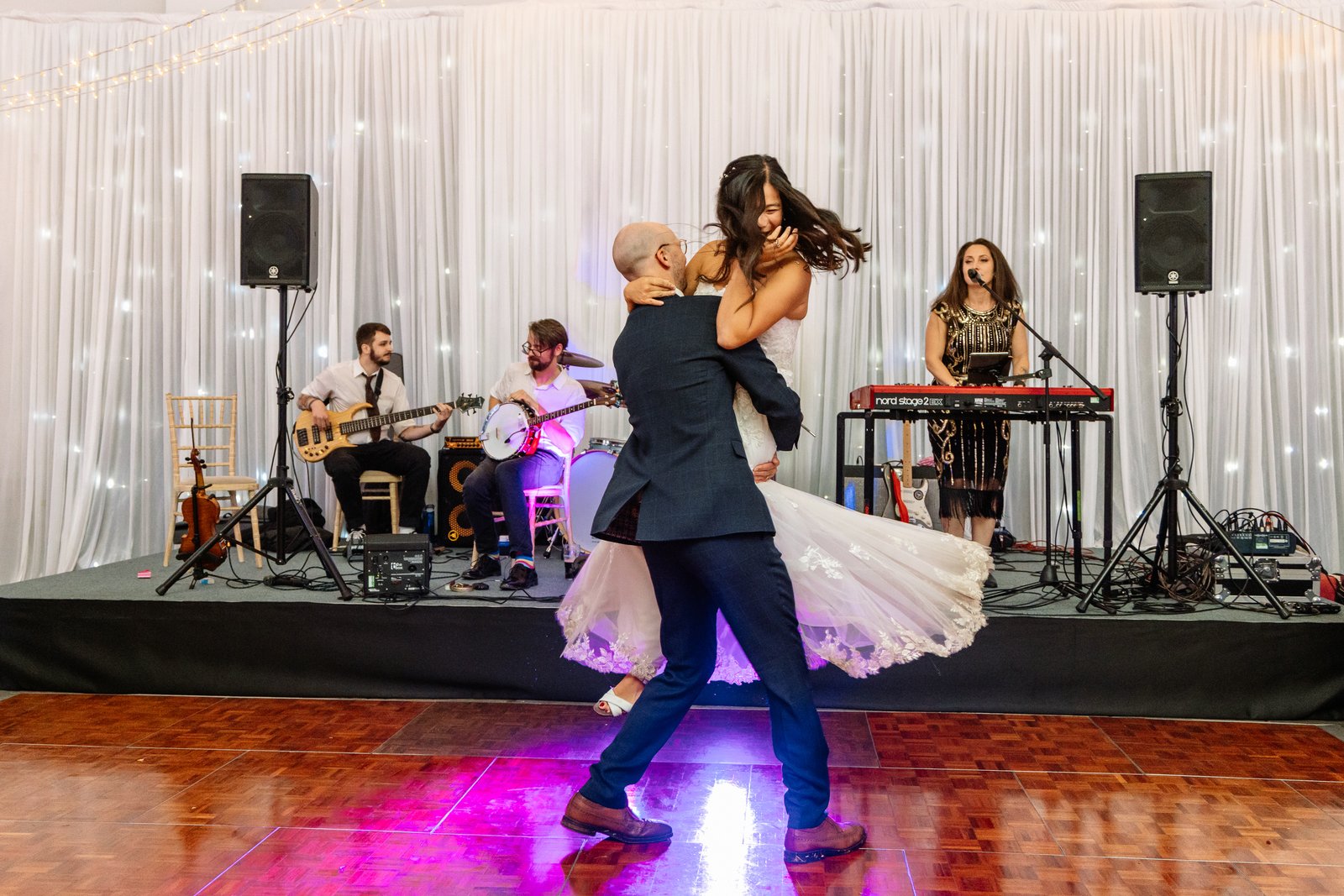 Bride and groom during their first dance in front of a live band, her dress spinning out.