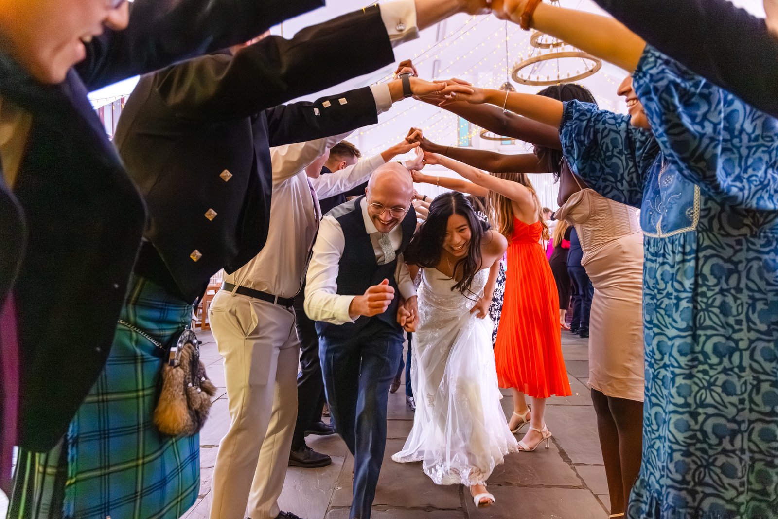 Guests forming an arch of raised hands for the couple during the ceilidh.