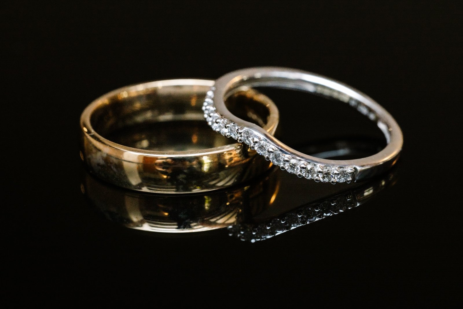 The couple's two wedding rings photographed close up on a dark reflective surface.