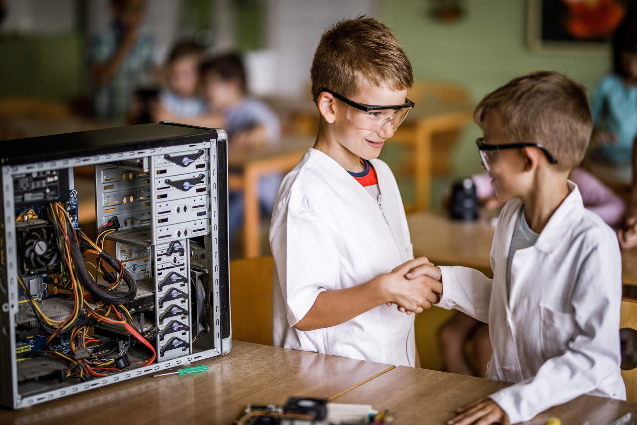 Two happy kids shaking hands in a classroom.