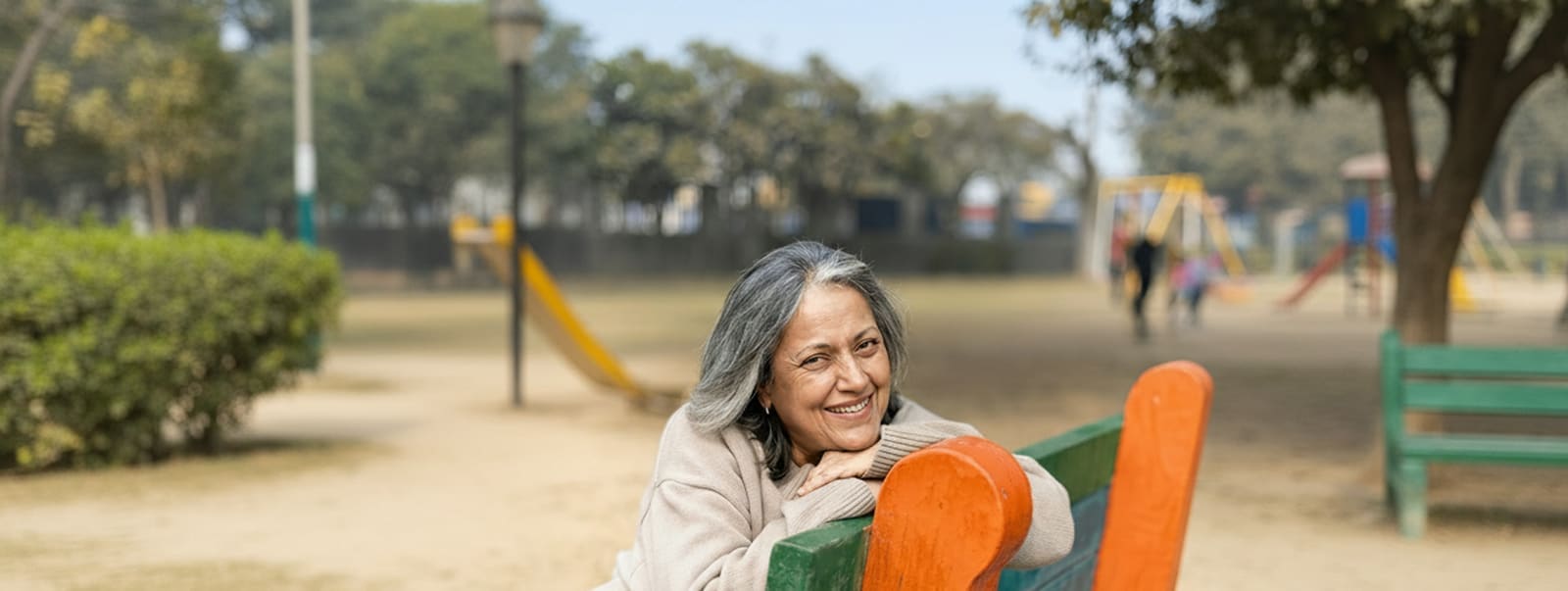 An older woman resting on a bench in a park, smiling