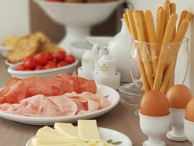 Un buffet de petit-déjeuner à ILICE B&B avec charcuterie, œufs, fromage et tomates cerises dans un cadre accueillant.