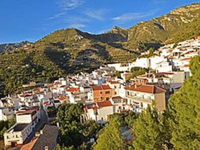 Panoramic view of Lentegí, with its white houses bordered by lush green mountains under a clear blue sky.
