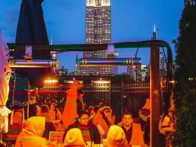 Lively atmosphere at the 230 Fifth Rooftop, with a view of the Empire State Building illuminated at dusk.