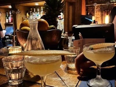 Two cocktails on a wooden bar at the Discount Suit Company, surrounded by glasses and a warm atmosphere.