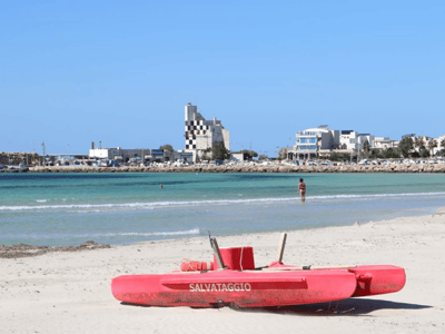 Plage de Torre San Giovanni avec des canots de sauvetage, eaux turquoise et bâtiments modernes en arrière-plan.