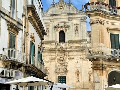 Architecture baroque de l’église à Martina Franca, entourée de bâtiments anciens et d’un café en plein air.