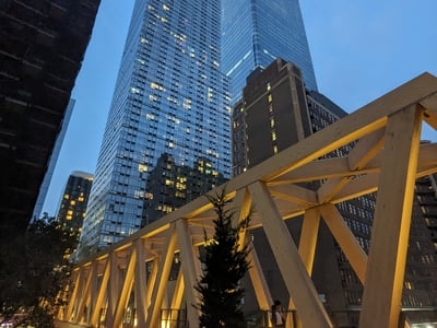 View of the illuminated Moynihan Train Connector, surrounded by modern skyscrapers in New York at dusk.