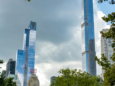 Gratte-ciels modernes se reflétant dans les nuages au-dessus de Central Park, créant un contraste saisissant avec la verdure.