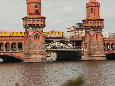 Pont emblématique d'Oberbaum à Warschauer Straße, avec un train passant au-dessus et le fleuve en arrière-plan.