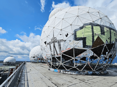 Abandoned spherical structures at Teufelsberg, Berlin, adorned with graffiti and overlooking a cloudy sky.