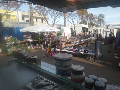 Sale of local and artisanal products at the local market, with colorful stalls under a sunny sky.