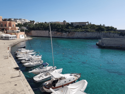 Boats moored in Tricase Porto, with crystal-clear waters and cliffs in the background, perfect for boating.