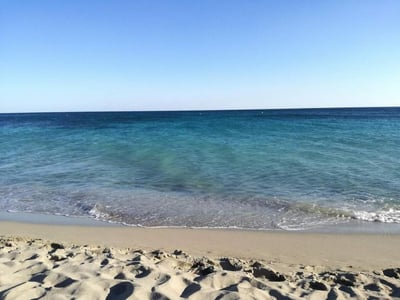 Peaceful beach with turquoise waters and a clear sky, close to the Mare Blu Apartments at Case Vacanze Villani.