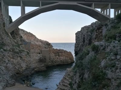 Modern bridge overlooking a rocky cove at Il Ciolo, illuminated by morning light.