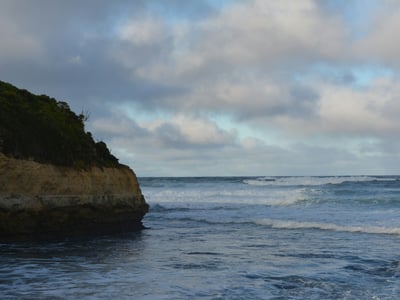Steep coast at Port Campbell, with waves gently crashing under a cloudy sky.