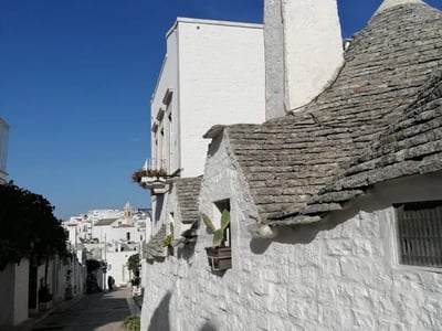 Narrow rue pavée du Quartier Monti, bordée de maisons blanches aux toits de pierre, sous un ciel bleu éclatant.
