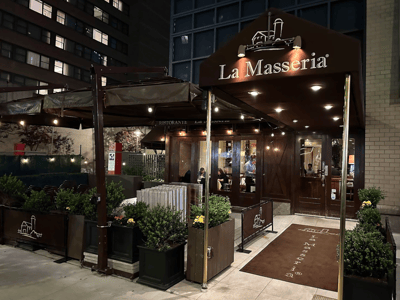 Entrée élégante du restaurant La Masseria, avec des plantes en pot et un éclairage chaleureux, prenant vie la nuit à New York.