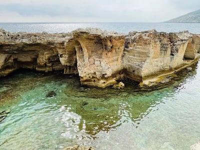 Majestic rock by the natural pool of Marina Serra, with crystal clear waters and a cloudy sky.