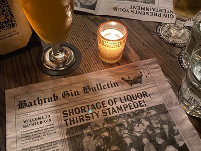 Bar room with a glass of beer, a lit candle, and a newspaper about the shortage of drinks at Bathtub Gin.