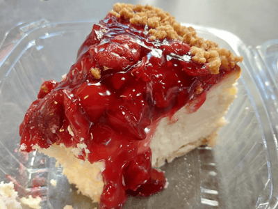 Junior's cheesecake slice, topped with cherry frosting and sauce, on a crispy crust base. A sweet delight to savor.
