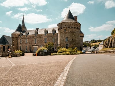Château historique à Sillé-le-Guillaume, avec des tours élancées et un paysage rural verdoyant en arrière-plan.