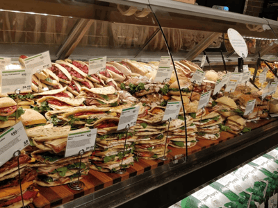 A varied selection of fresh sandwiches displayed in a counter at Whole Foods Market, with visible price tags.
