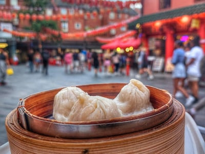 Delicious steamed dumplings in a bamboo basket, with lanterns and visitors from Chinatown in the background.