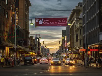 Busy street in Adelaide, decorated for Christmas, with cars and a colorful sky at dusk.