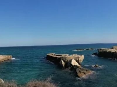 Crystal clear waters and rocks at Roca Vecchia, a soothing coastal landscape under a sunny sky.