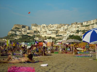 Lively beach in Peschici, bathed in sunshine, with colorful umbrellas and holidaymakers enjoying the sand and the sea.
