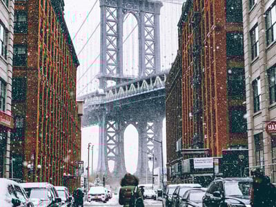 Snowy street in Brooklyn under the Manhattan Bridge, showing a winter atmosphere and historic architecture.