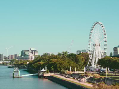 Vue panoramique de la roue de Brisbane, entourée de verdure, avec le fleuve et la ville moderne en arrière-plan.