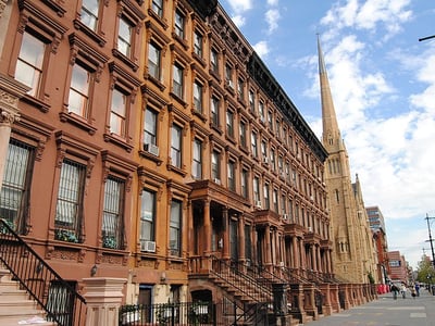 Historical architecture of Harlem with brown brick buildings and a tall spire church in the background.