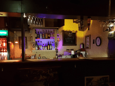 Madame Claude's bar with a shelf filled with bottles of alcohol and colorful lights creating a warm atmosphere.