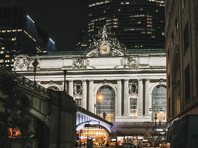 Illuminated facade of Grand Central Station, iconic to New York, surrounded by modern skyscrapers.