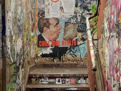 Colorful stairway of Haus Schwarzenberg in Berlin, adorned with posters and vibrant street art, representing alternative culture.
