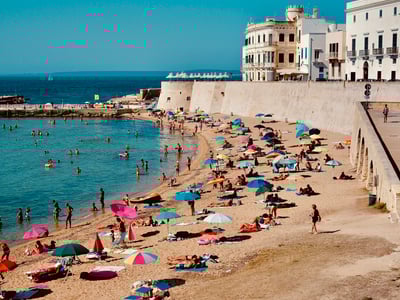 Lively beach of Gallipoli, with colorful umbrellas and bathers enjoying a beautiful sunny day by the sea.