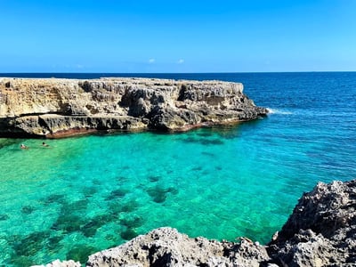 Eaux turquoise et falaises de Cala Copacabana sous un ciel bleu, idéal pour les activités nautiques et la détente.