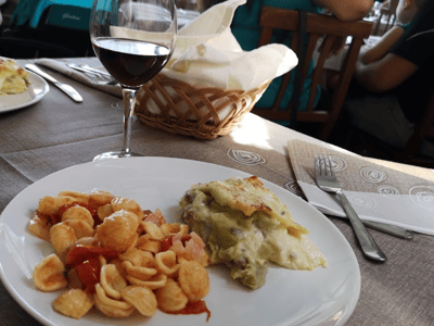 Délicieux plat de pâtes orecchiette et lasagne, accompagné d'un verre de vin rouge, servi au restaurant Le Fontanelle.