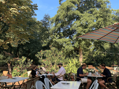 Friendly terrace of the Café am Neuen See, where customers enjoy drinks in a green and relaxing setting.